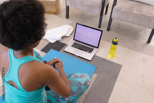 African american mid adult woman using practicing yoga through laptop at home