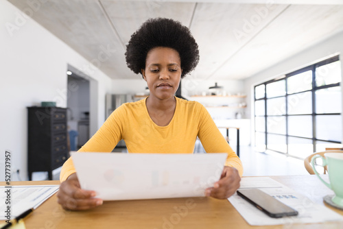 African american mid adult female freelancer analyzing chart while sitting at desk in home office