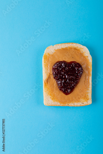Overhead view of preserves and peanut butter on bread slice over blue background with copy space