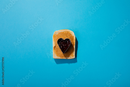 Overhead view of jam in heart shape pastry cutter over bread with peanut butter on blue background