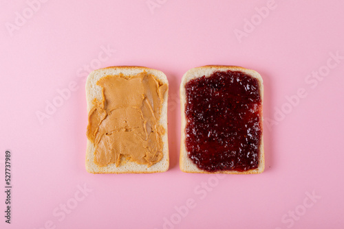 Directly above shot of peanut butter and preserves on bread slices over pink background