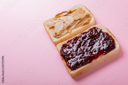 Close-up of peanut butter and preserves on bread slices over pink background