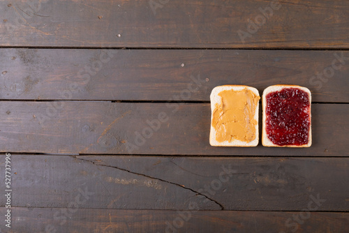 Overhead view of bread slices with peanut butter and preserves on wooden table with empty space
