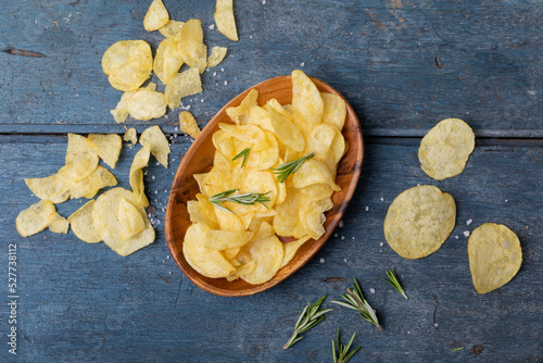 Overhead view of potato chips in bowl with rosemary and salt on wooden table