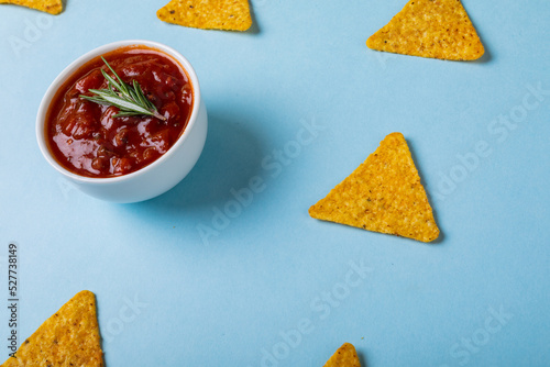 High angle view of red sauce with rosemary by nacho chips over blue background