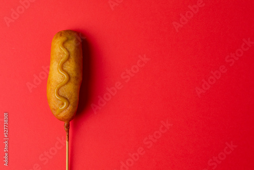 Overhead close-up shot of corn dog with mustered sauce over skewer on red background with copy space