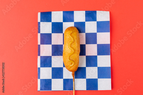Directly above shot of corn dog with mustard sauce on checked pattern paper over red background