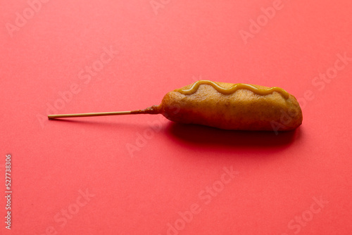 Close-up shot of corn dog with mustered sauce over skewer on red background with copy space