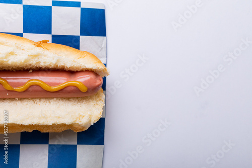 Hot dog with mustered sauce on checked pattern paper over white background with copy space