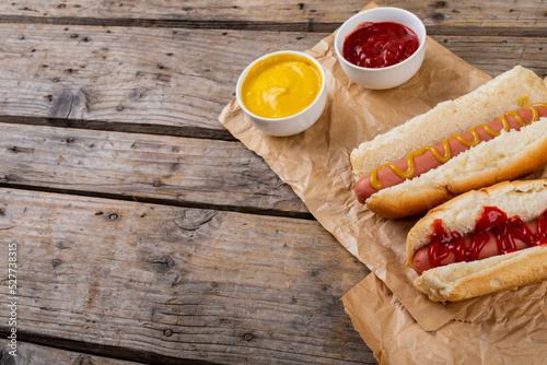 High angle view of hot dogs with tomato and mustered sauces on paper bags at table