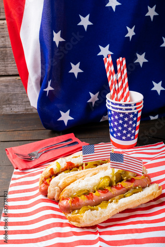 Hot dogs served with jalapenos against american flag with fork, straw and disposable cups at table