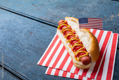Close-up of hot dog with tomato, mustered sauce and american flag on paper at table
