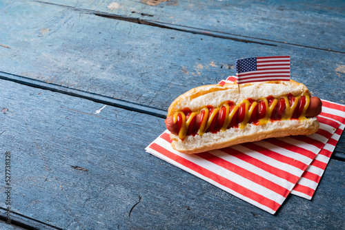 High angle view of hot dog with tomato, mustered sauce and american flag on paper at table