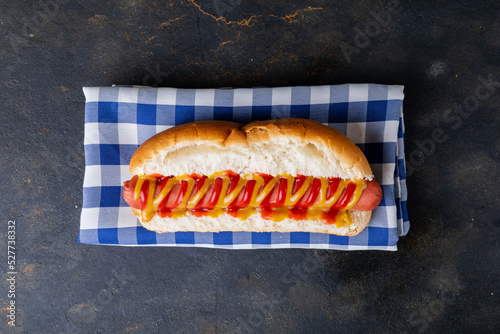 Overhead view of hot dog with tomato and mustered sauce on checked pattern napkin at table
