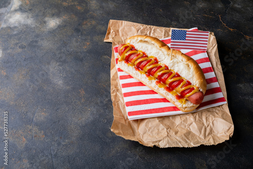 American flag on hot dog with mustered and tomato sauce on brown wax paper at table