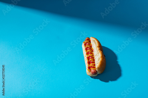 Close-up of hot dog with mustered and tomato sauce against blue background with copy space