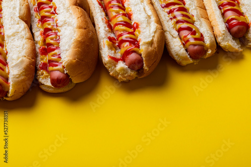 High angle view of sauces on hot dogs arranged side by side on yellow background