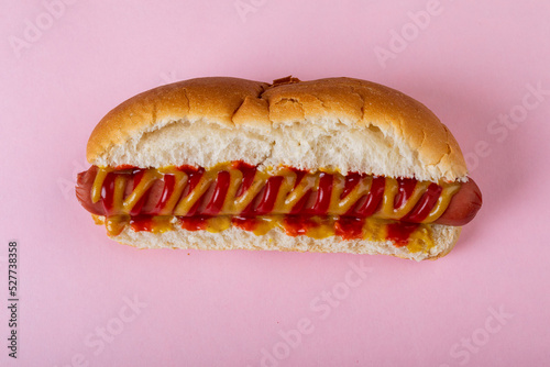 Overhead close-up of mustered sauce and tomato sauce on hot dog over pink background