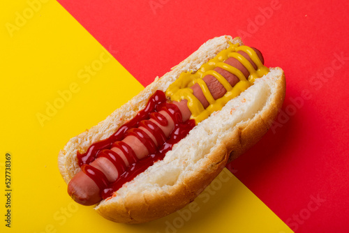 Close-up of hot dog with mustered and tomato sauce on two tone background with copy space