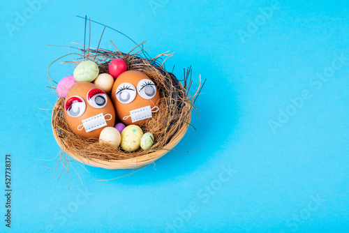 High angle view of easter eggs with mask and doodle eyes with candies in nest on blue background