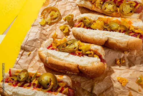 High angle view of hot dogs with sauces and jalapeno on brown wax paper over yellow background