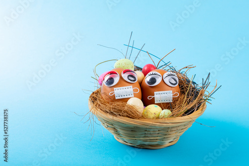 Close-up of easter eggs with doodle eyes and mask with candies and straws in nest on blue background