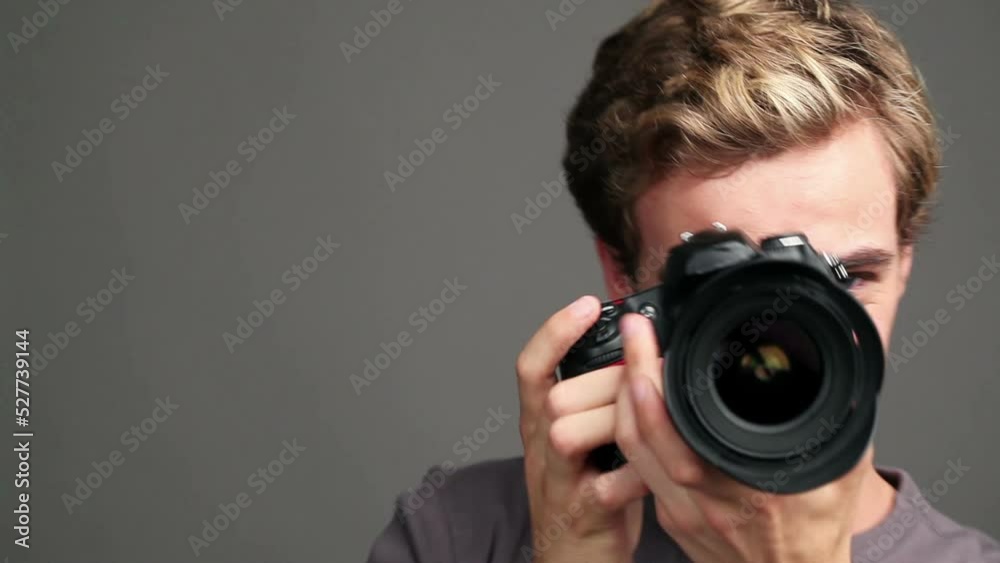 Professional photographer talking and taking photo with camera against a grey studio background. Happy creative artist or man with smile enjoy photography job with technology or gear during a shoot Professional photographer talking and taking photo with camera against a grey studio background. Happy creative artist or man with smile enjoy photography job with technology or gear during a shoot