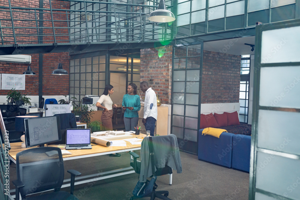 Multiracial young male and female architects discussing while standing in modern office Multiracial young male and female architects discussing while standing in modern office