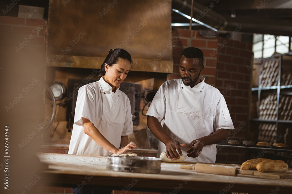 Asian mid adult female baker showing dough kneading to african american mid adult male coworker Asian mid adult female baker showing dough kneading to african american mid adult male coworker