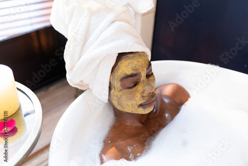High angle view of african american woman with face mask relaxing in bath tub at home photo