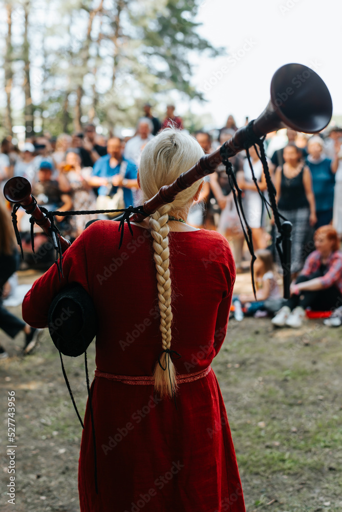 Folk concert outdoors. Back view of a woman musician in a medieval costume playing the bagpipes