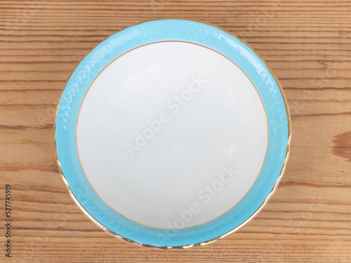 Top view of a small ceramic plate, white on the inside and blue on the edge on wooden background