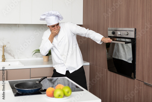 Fotografie Young inexperienced cooker trying to open the oven but something going wrong