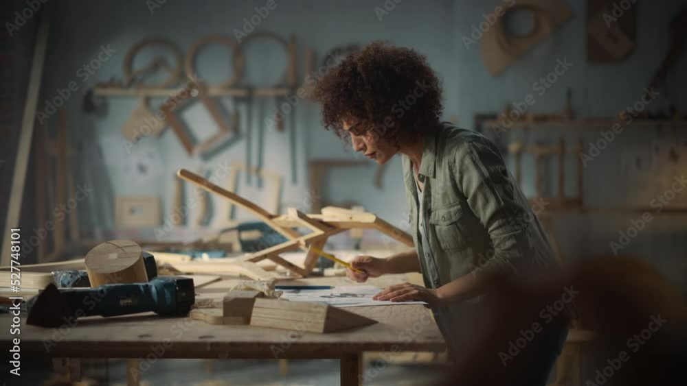 Portrait of a Young Beautiful Carpenter Checking a Blueprint and Starting to Assemble a Wooden Chair. Professional Furniture Designer Working in a Studio in Loft Space with Tools on the Walls.