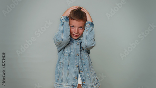 Stressed depressed toddler boy 10 years old expresses his fear and waves his hands away from danger, waving no. Scared fearful children teenager child isolated alone on gray studio wall background
