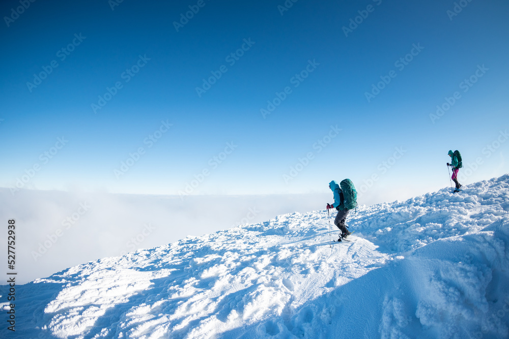 Two women with backpacks walk in snowshoes in winter trekking