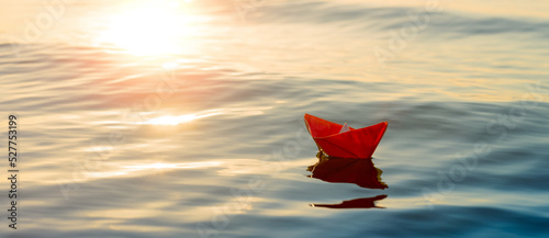 Tela paper boat sails into the sea, a small origami ship on the water in the setting sun, travel concept