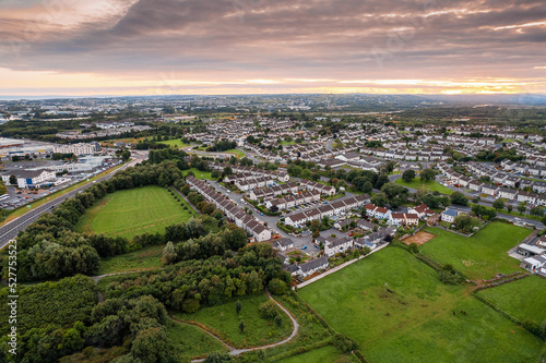 Aerial view on high dense residential area at sunset. House estate by a small park with green trees and fields. Modern family houses with car park and backyard. Galway, Ireland.