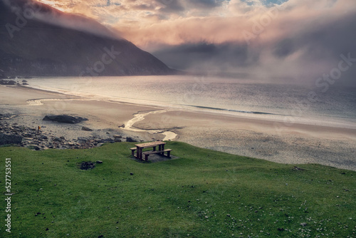 Table and benches for tourist on a grass with stunning view on Keem bay and beach early in the morning. Low clouds and fog over ocean and mountain. Ireland. Famous travel area. Irish landscape. © mark_gusev