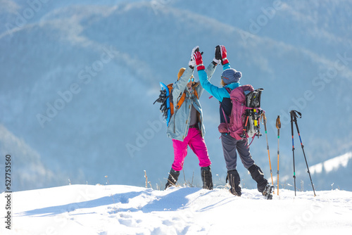 two women climbed to the top of the mountain during a winter hike, girl gives high five to friend