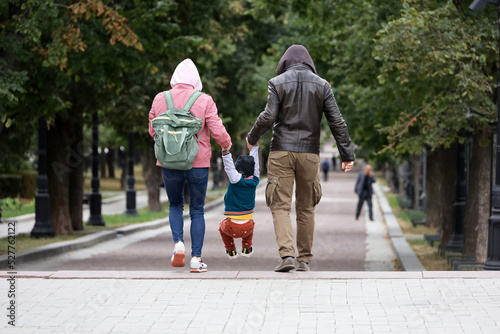 Young couple with kid boy walking on a street holding his hands, family leisure in autumn city