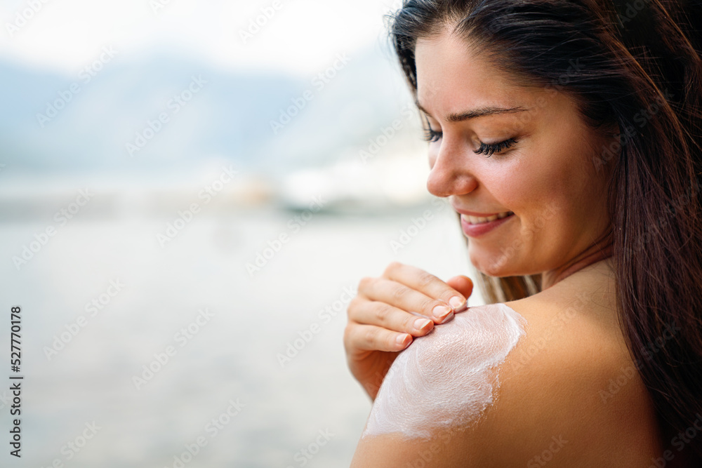Attractive woman with healthy skin applying sunscreen to shoulder on summer vacation at beach Attractive woman with healthy skin applying sunscreen to shoulder on summer vacation at beach