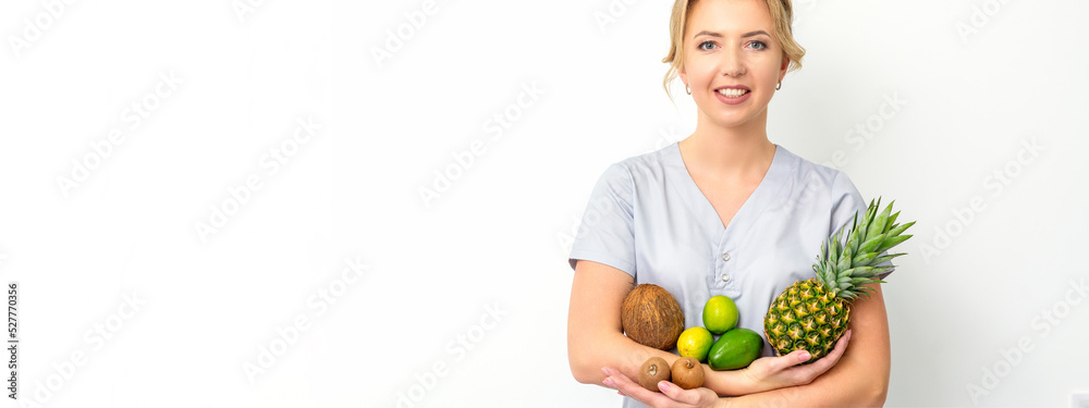 Portrait of a young caucasian smiling female nutritionist with different fruits in her hands over white background Portrait of a young caucasian smiling female nutritionist with different fruits in her hands over white background