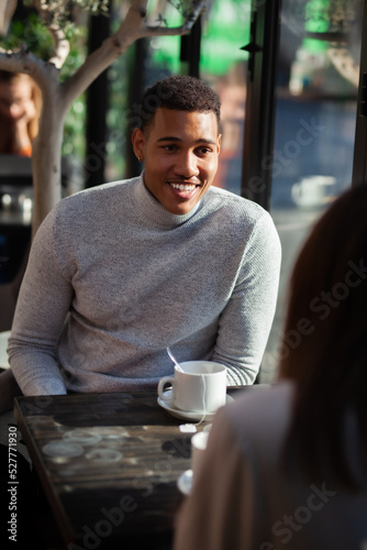 Two friends in a restaurant talking smiling and drinking tea. Multuracial business colleagues having a meeting after work or during coffee break at a cafe bar. Freelance lady working in the background photo