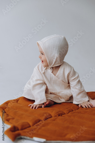 Cute studio portrait of a little newborn girl posing for a photo on a light background. A baby who has already learned to crawl and sit