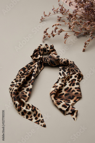 Close-up shot of a leopard hair scarf scrunchie. The animal print hair band is isolated on a pastel background with dried flowers. Top view.