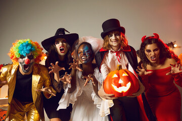 Group of young people dressed up as spooky characters having fun at Halloween costume party. Adult male and female friends with scary makeup on faces doing claw gesture, hissing and making grimaces