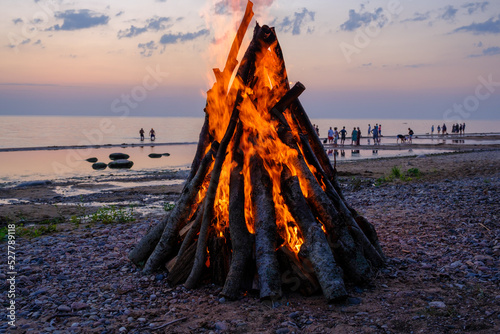 Fototapeta Naklejka Na Ścianę i Meble -  A bonfire on the shore of the Baltic Sea. People at sunset by the sea. Riga Gulf