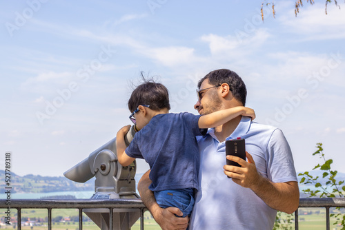 happy kid and father taking selfie on beautiful view mountains landscape summer vacation time.travel adventure family together.smiling dad and son selfie with phone camera.daddy hold in arms boy