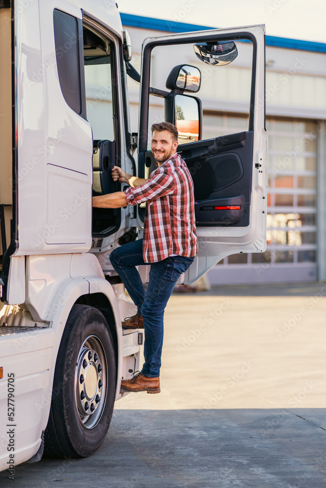 Photo of motivated smiling middle aged truck driver entering his semi truck long vehicle. Happy trucker. Transportation service. Photo of motivated smiling middle aged truck driver entering his semi truck long vehicle. Happy trucker. Transportation service.